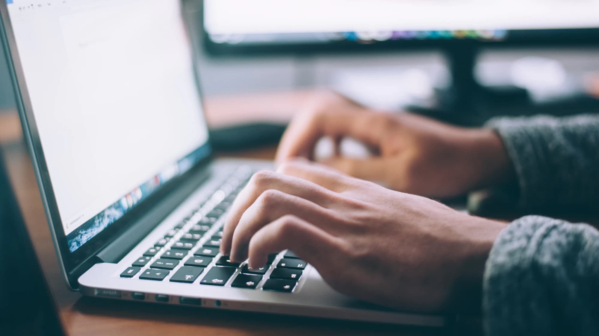 Hände tippen auf der Tastatur eines Laptops an einem Arbeitsplatz